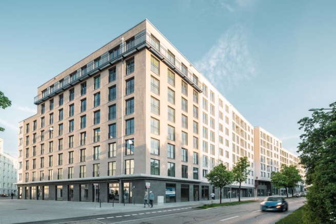 Architekturfotografie einer Wohnanlage im Abendlicht, Passanten und Verkehr in Bewegung.